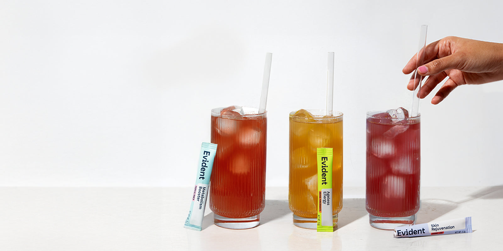 Three glasses of iced drinks with straws and Evident brand packets on a white background