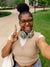 Person wearing a beige sweater vest and glasses, making a peace sign outdoors.