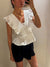 Person wearing a white ruffled top and black shorts against a plain background