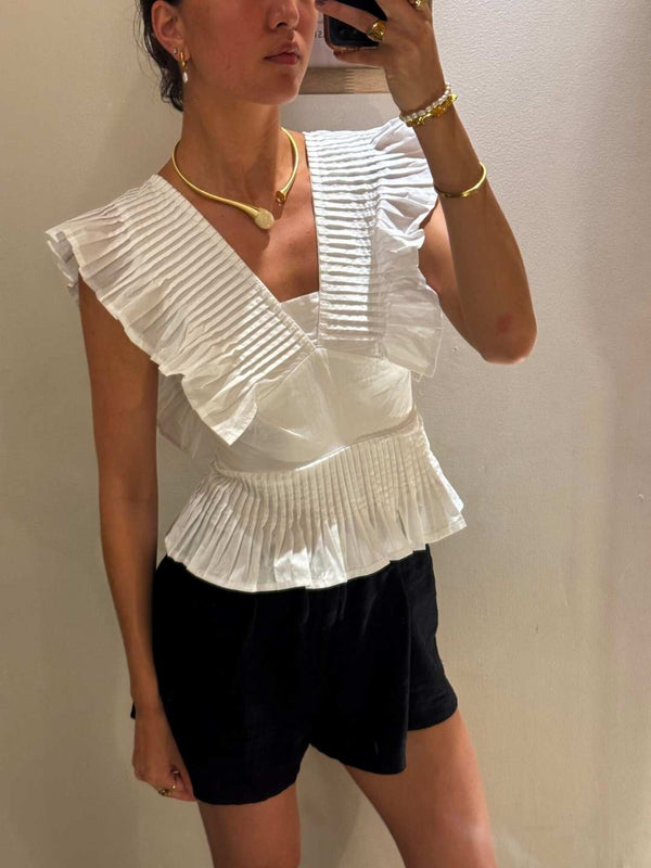 Person wearing a white ruffled top and black shorts against a plain background