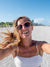 Woman taking a selfie on a beach with sunglasses and a white top