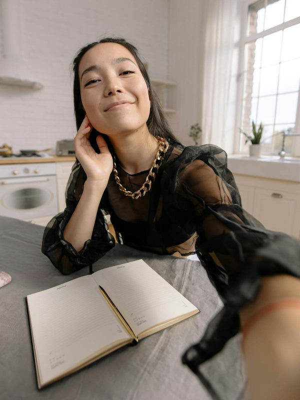 Person taking a selfie in a kitchen with an open notebook on the table