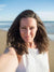 Woman taking a selfie on a beach with ocean and sky in the background
